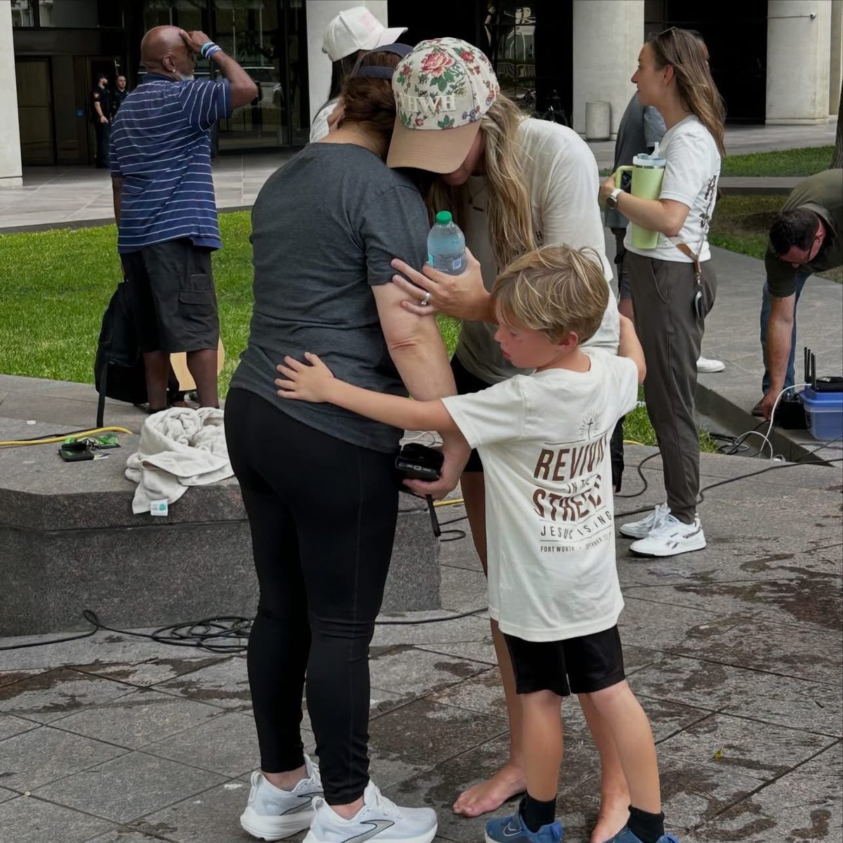 Kelsey embracing a woman in prayer while a young boy lays his hand on her