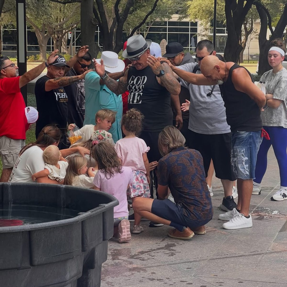 A circle of people laying hands and praying over others, with children kneeling in the center