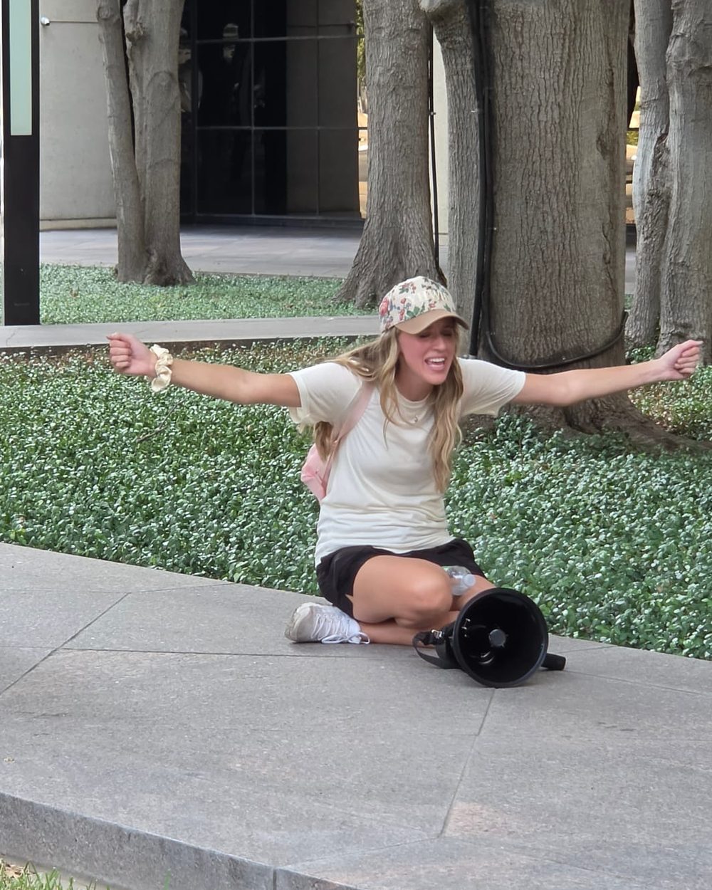 Kelsey Trujillo sitting on the lawn with her arms open wide in worship