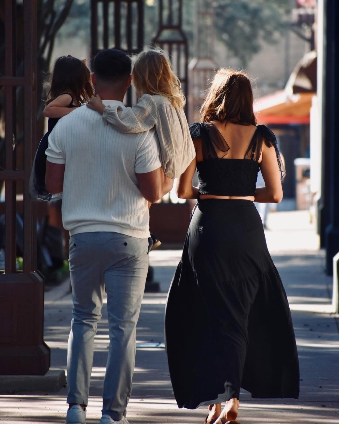Nash carrying his daughters Sage and Hazel, with Kelsey walking beside them, photographed from behind